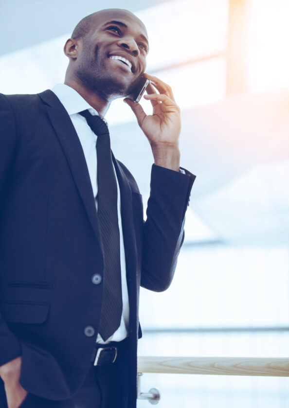 Good budiness talk. Low angle view of cheerful young African man in formalwear talking on the mobile phone and smiling